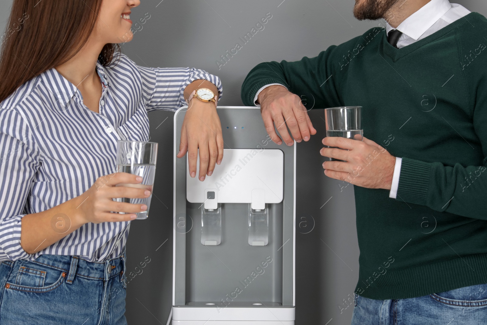 Photo of Employees with glasses near water cooler in office