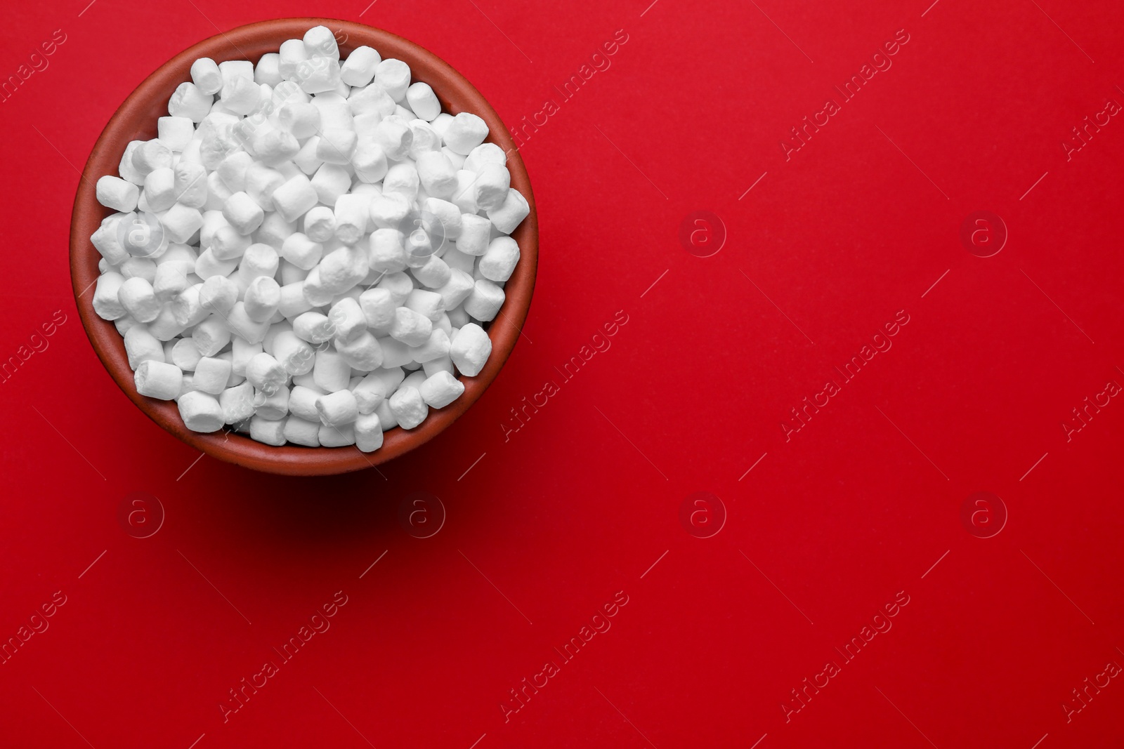 Photo of Bowl with delicious marshmallows on red background, top view. Space for text