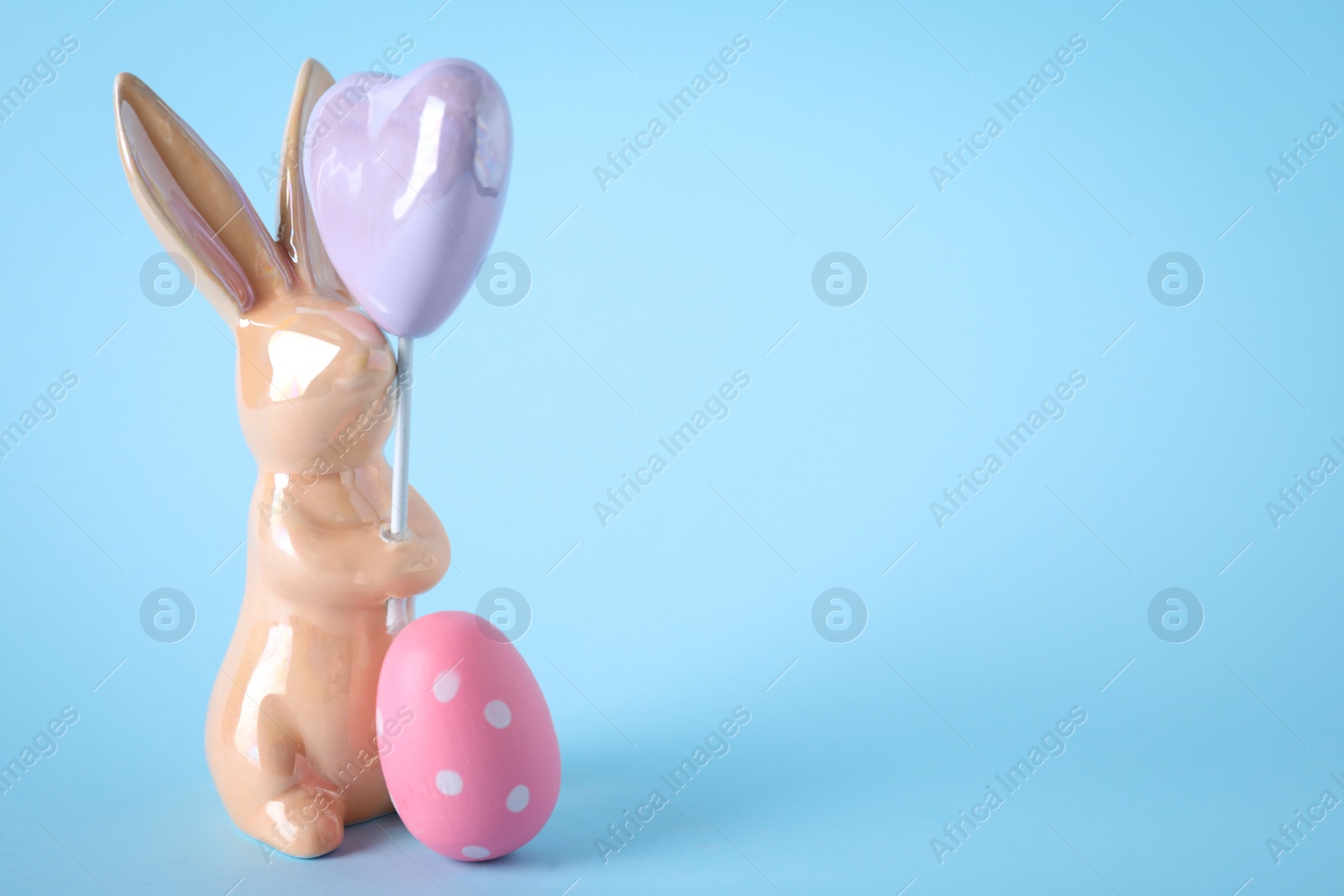 Photo of Easter bunny figure and dyed egg on light blue background. Space for text