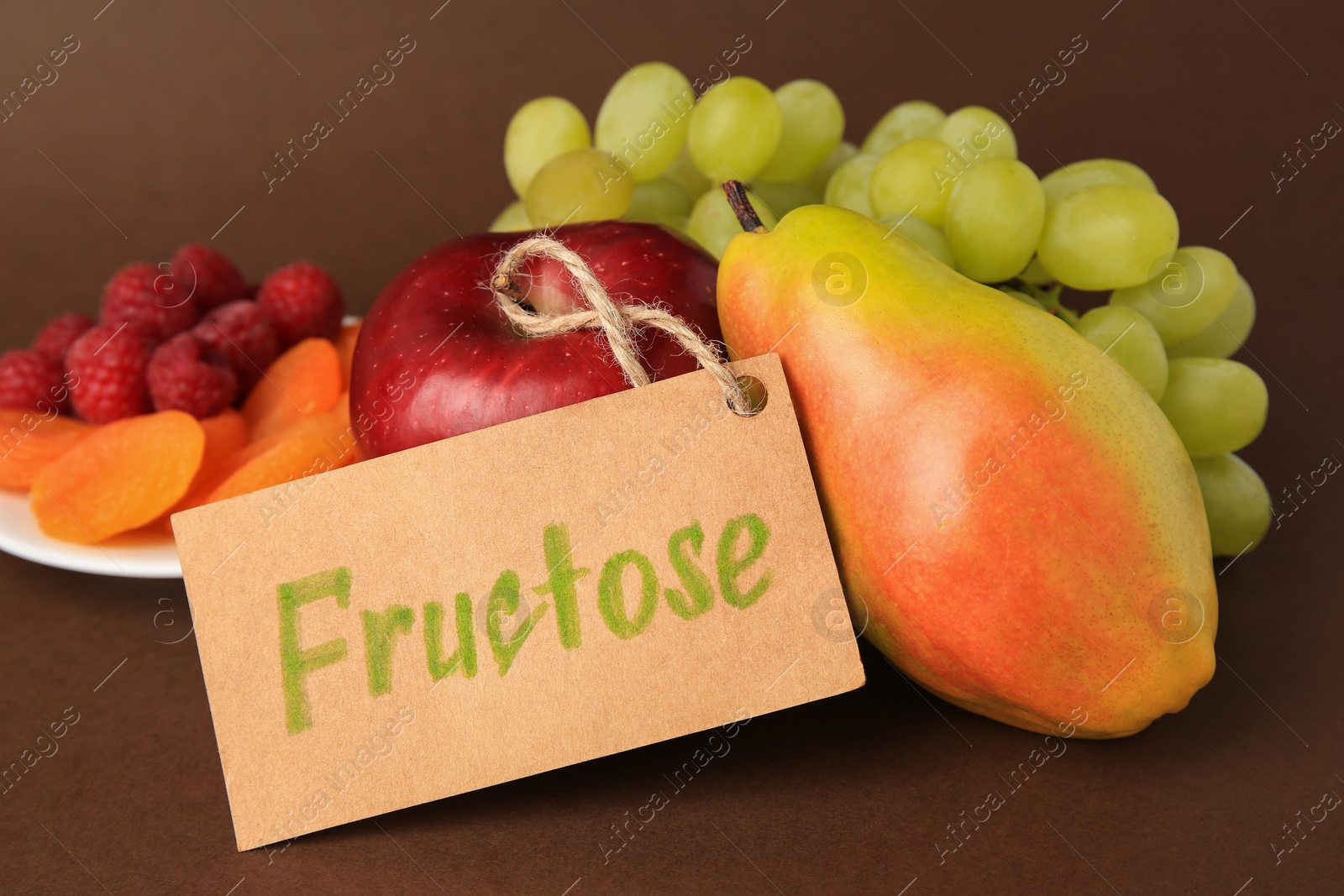 Photo of Card with word Fructose, delicious ripe fruits, raspberries and dried apricots on brown background, closeup
