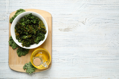 Photo of Tasty baked kale chips on white wooden table, top view. Space for text