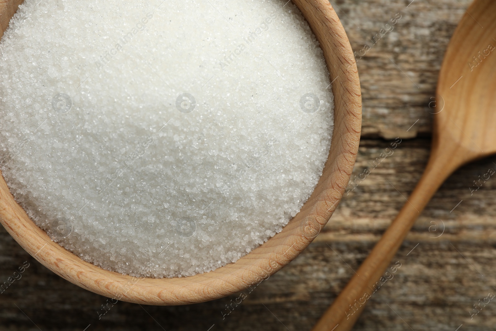 Photo of Granulated sugar in bowl and spoon on wooden table, top view