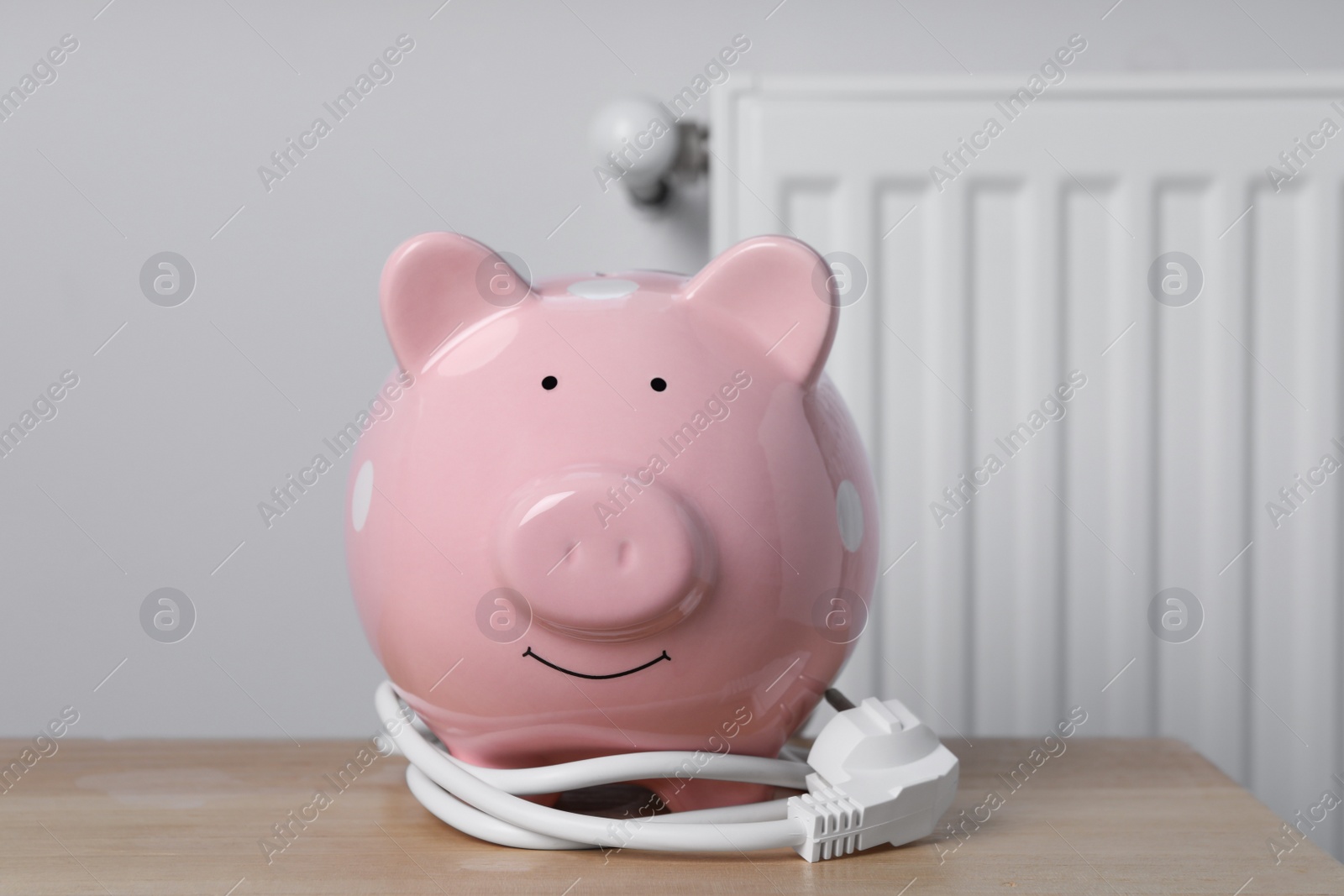 Photo of Piggy bank with plug on wooden table near heating radiator