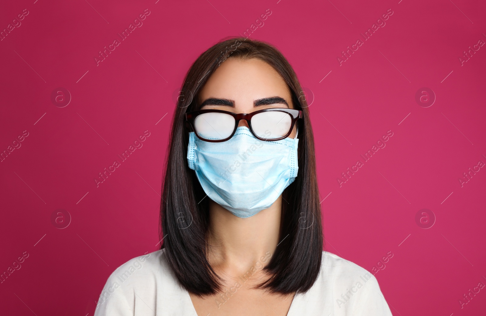 Photo of Young woman with foggy glasses caused by wearing disposable mask on pink background. Protective measure during coronavirus pandemic