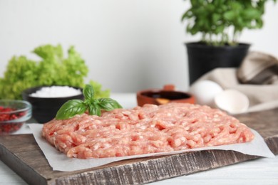 Raw chicken minced meat with basil on white wooden table, closeup