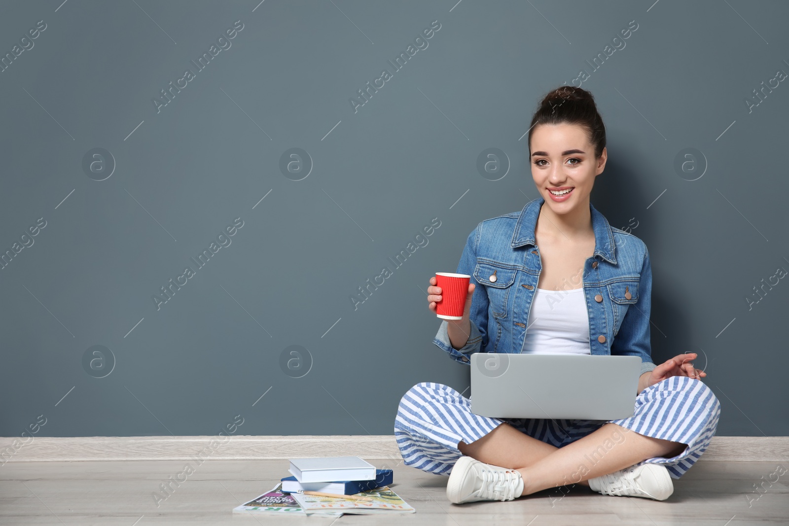 Photo of Young blogger with laptop sitting on floor near color wall