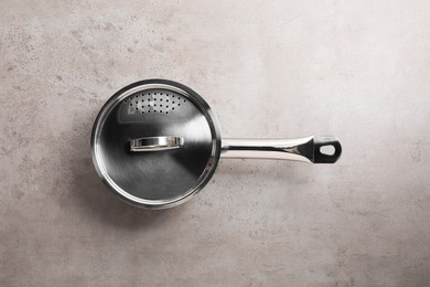 Photo of One steel saucepan with strainer lid on light textured table, top view