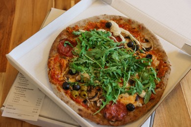 Delicious pizza with arugula, mushrooms and olives in box on wooden table, above view