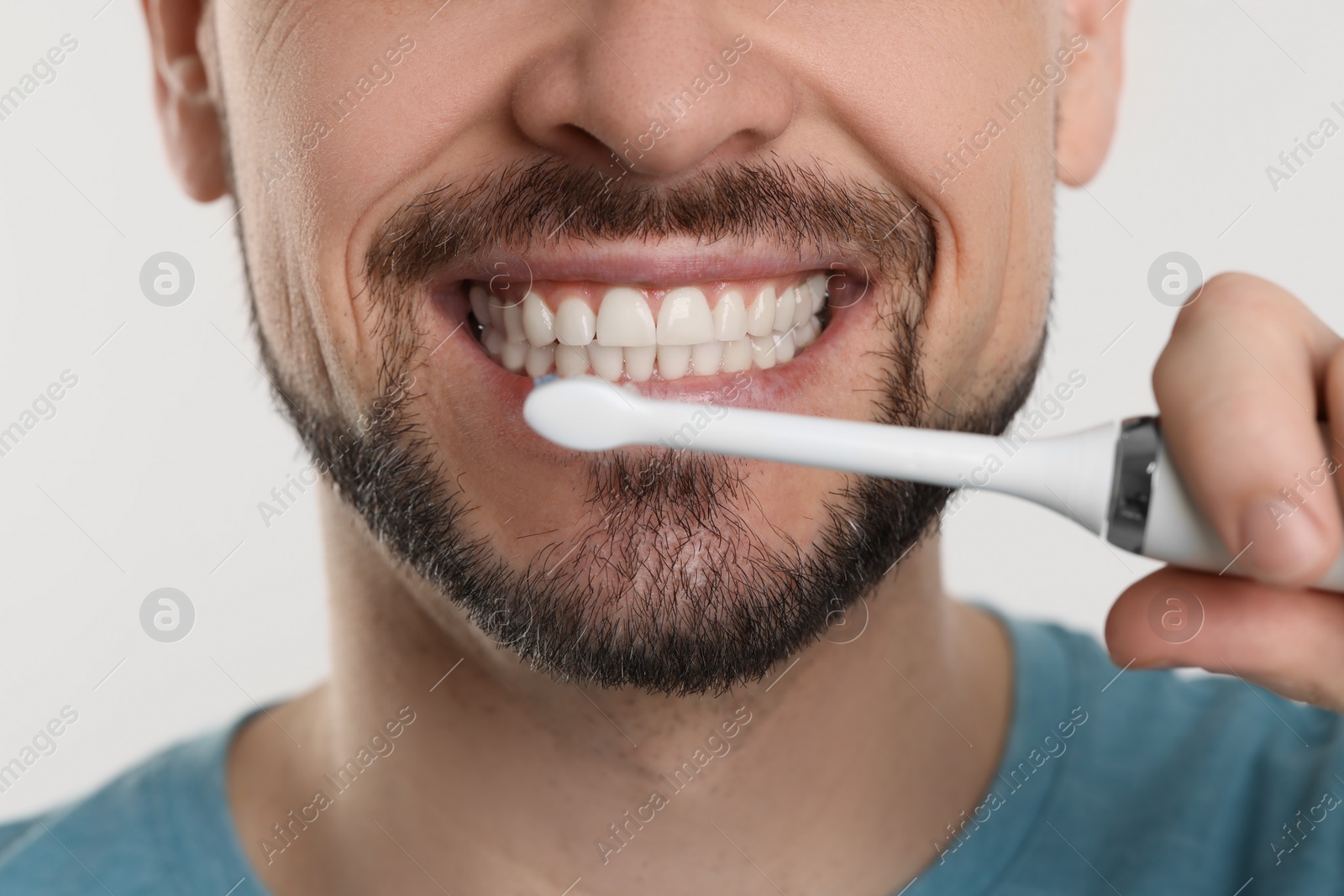 Photo of Man brushing his teeth with electric toothbrush on white background, closeup