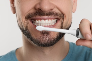 Photo of Man brushing his teeth with electric toothbrush on white background, closeup