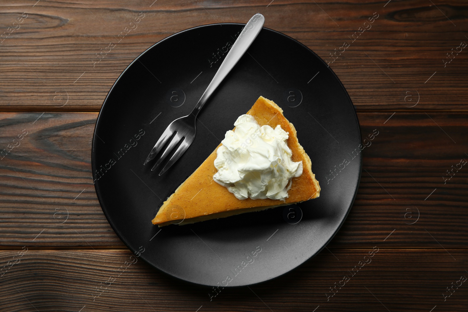 Photo of Piece of delicious pumpkin pie with whipped cream and fork on wooden table, top view