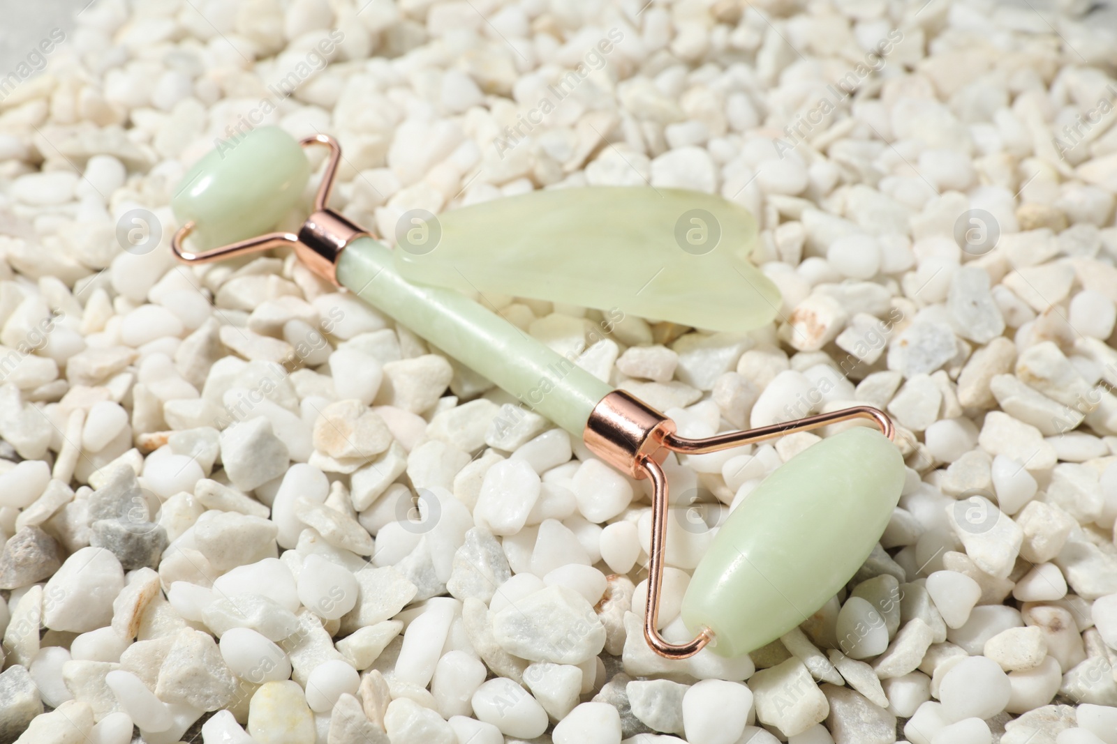 Photo of Quartz gua sha tool and face roller on white stones, closeup