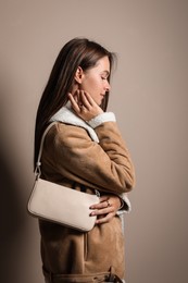 Fashionable young woman with stylish bag on beige background