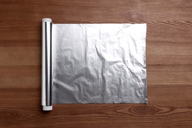 Photo of Roll of aluminum foil on wooden table, top view