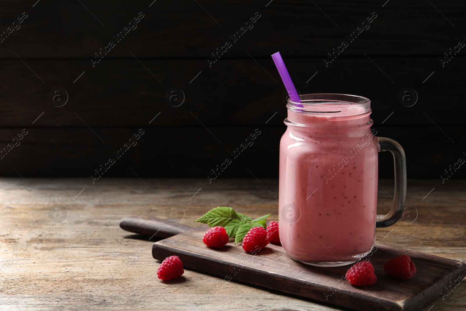 Image of Yummy raspberry smoothie in mason jar on wooden table. Space for text
