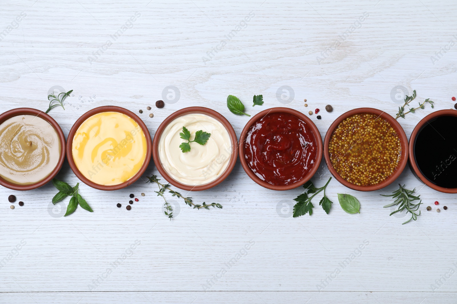 Photo of Many different sauces and herbs on white wooden table, flat lay