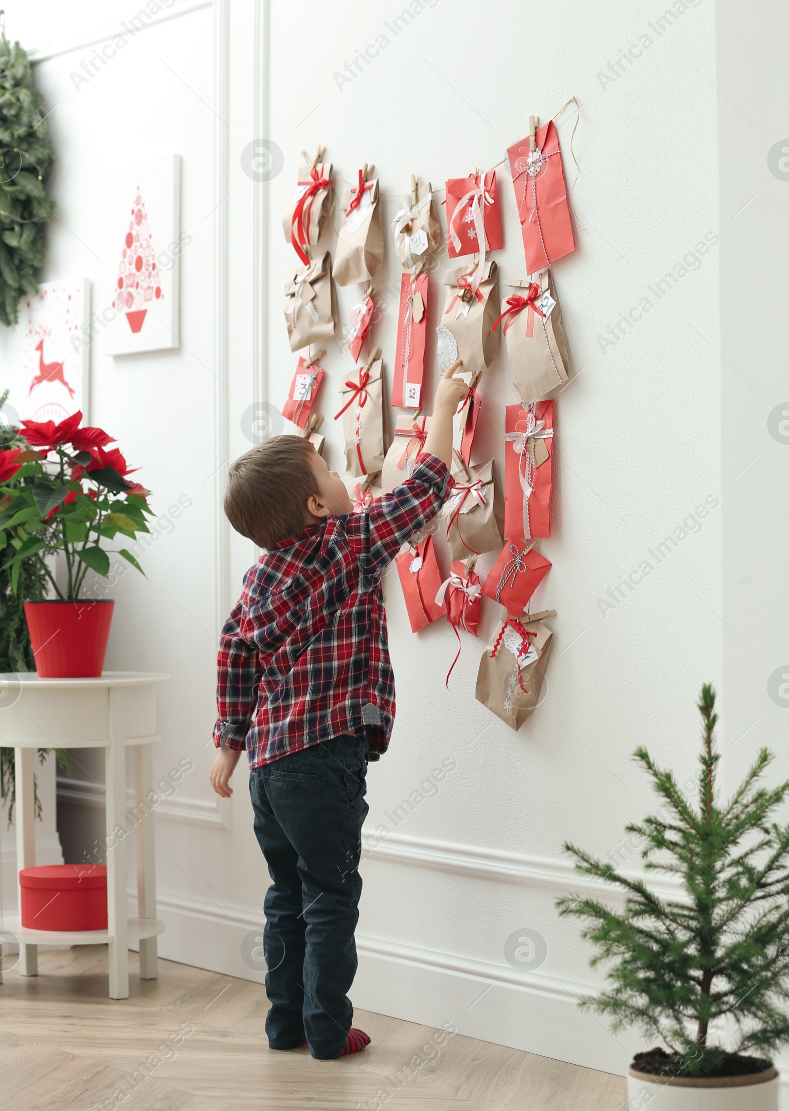 Photo of Cute little boy taking gift from Advent calendar at home. Christmas tradition