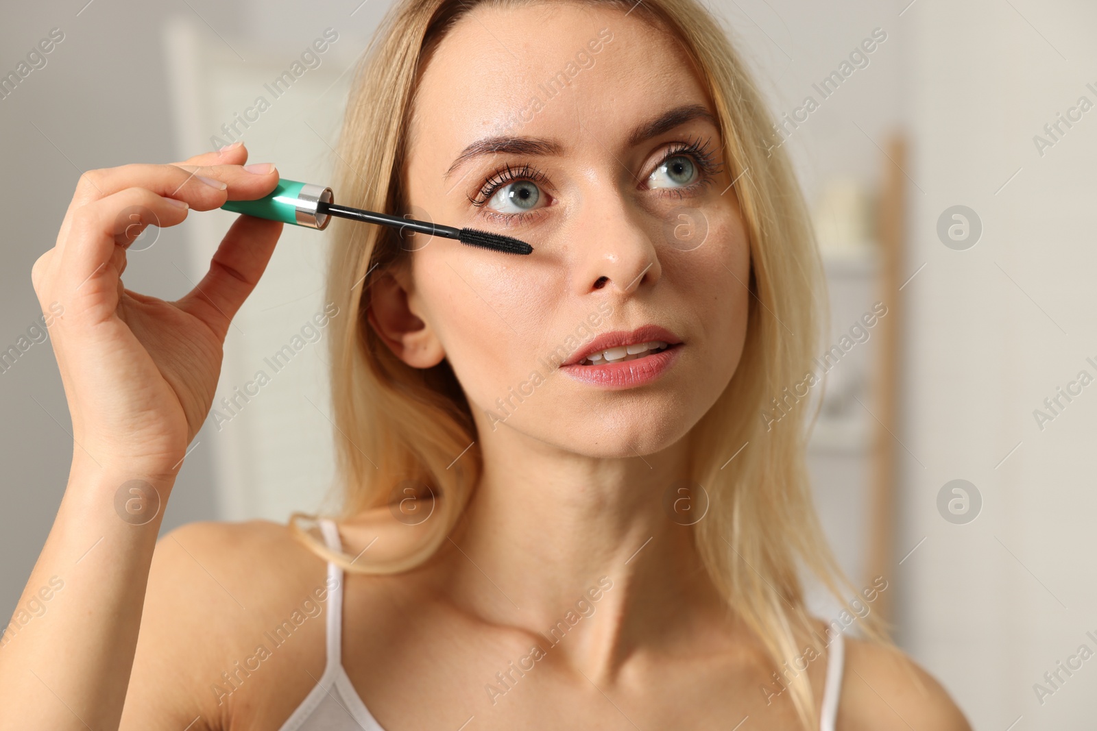 Photo of Beautiful woman applying mascara with brush indoors, closeup