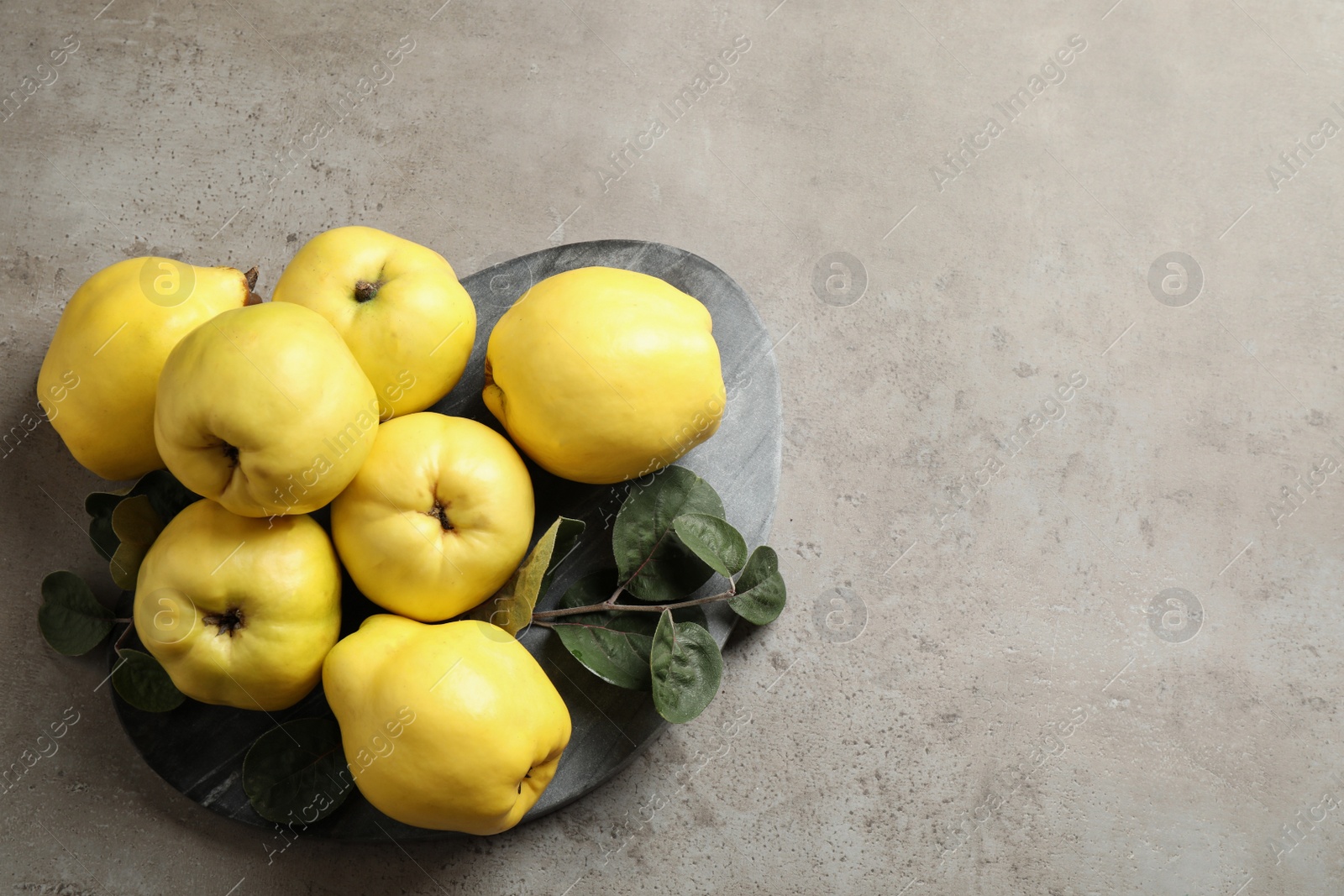 Photo of Fresh ripe organic quinces with leaves on grey table, flat lay. Space for text