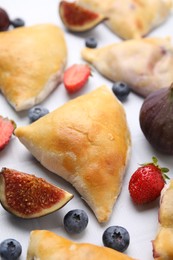 Photo of Delicious samosas, berries and fig on white tiled table, closeup