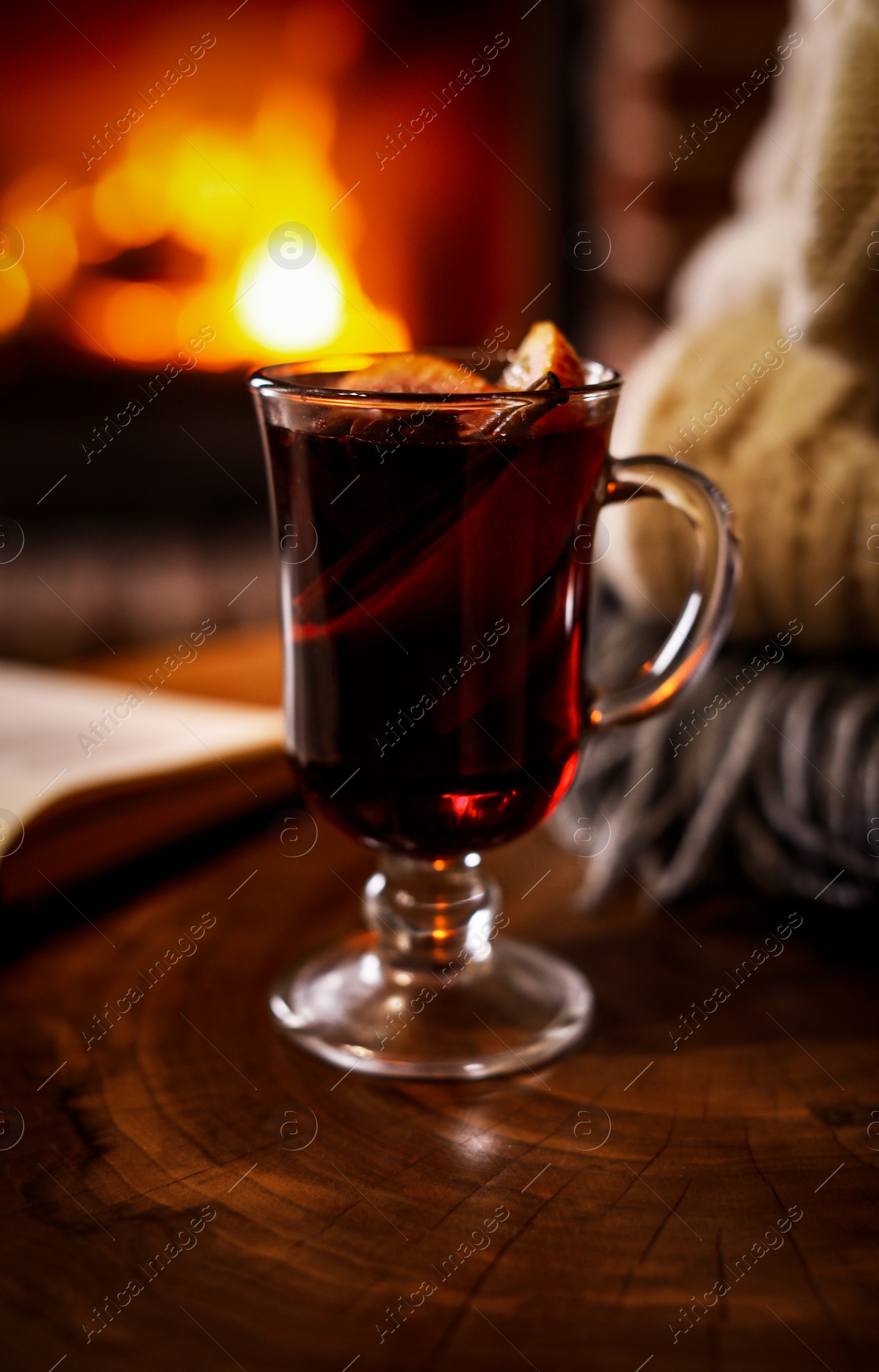 Photo of Tasty mulled wine, book, knitwear and blurred fireplace on background