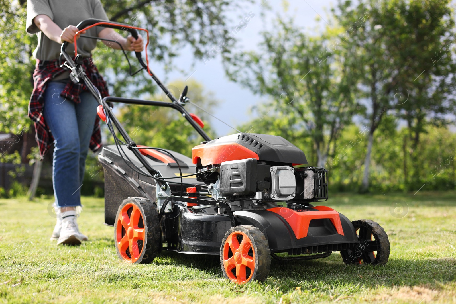 Photo of Woman cutting green grass with lawn mower in garden, selective focus