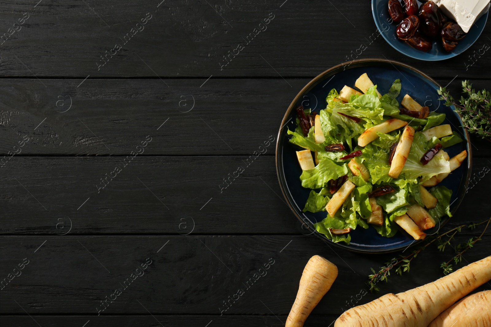 Photo of Delicious parsnip with lettuce and dates on black wooden table, flat lay. Space for text