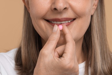 Photo of Senior woman taking pill on beige background, closeup