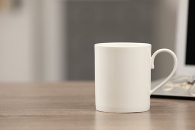 White ceramic mug and laptop on wooden table at workplace. Space for text