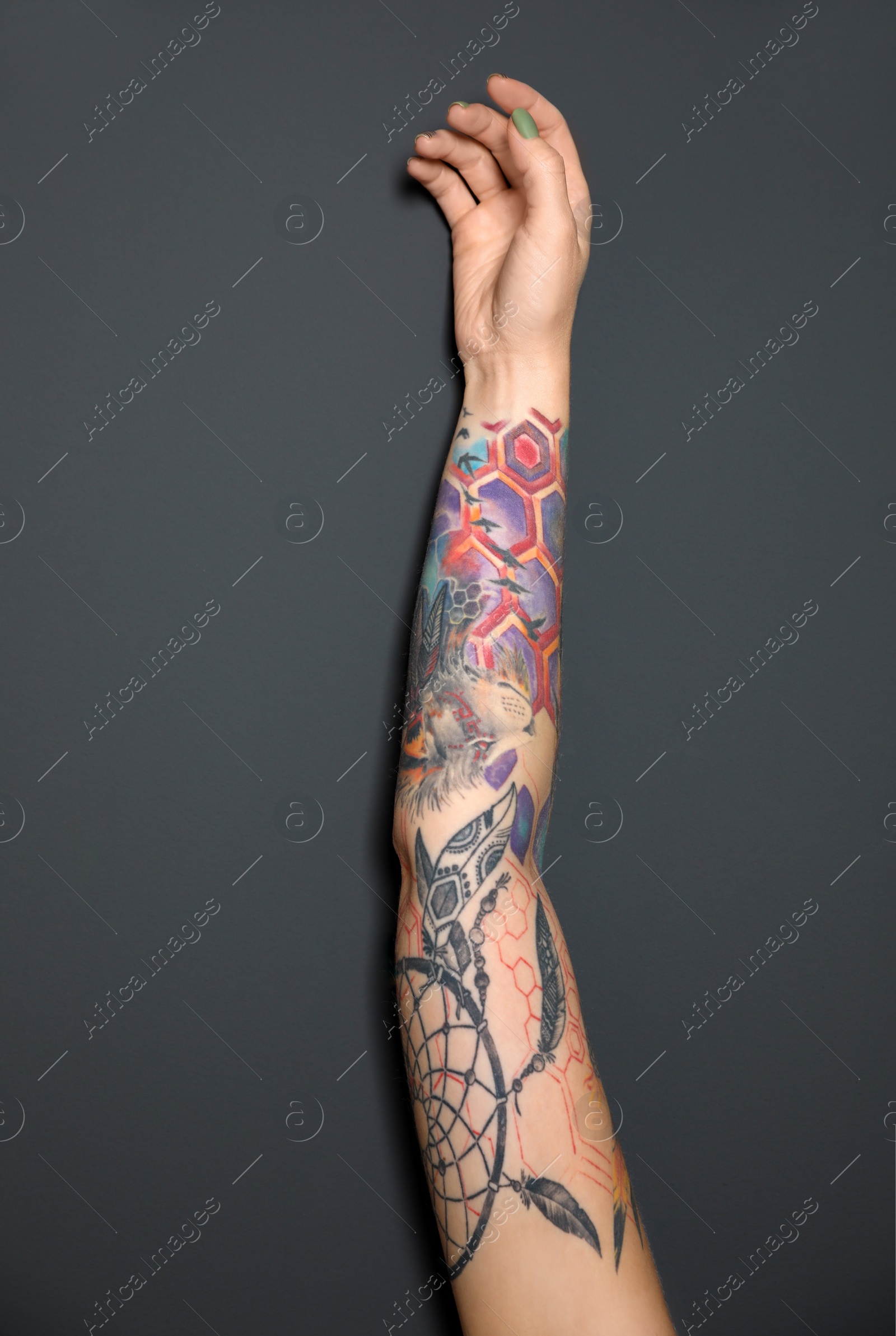 Photo of Woman with colorful tattoos on arm against dark grey background, closeup