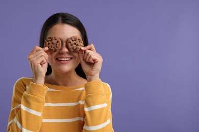 Young woman with chocolate chip cookies on purple background, space for text