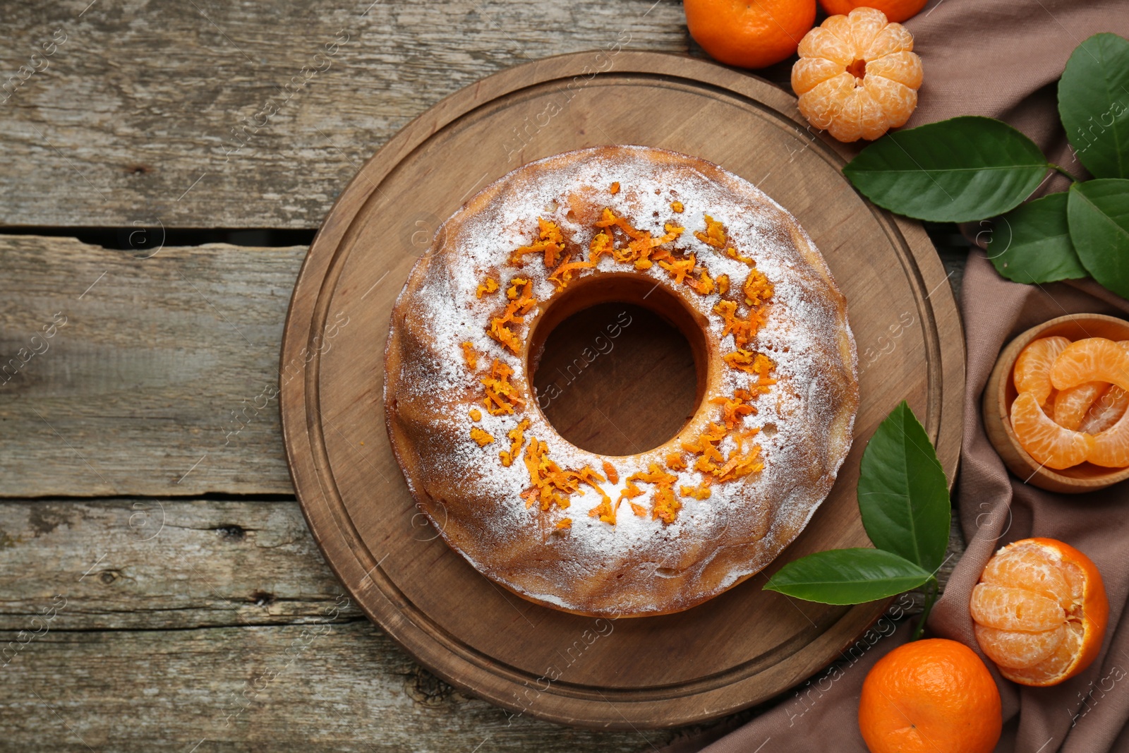 Photo of Homemade yogurt cake with tangerines, powdered sugar and green leaves on wooden table, flat lay