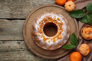 Photo of Homemade yogurt cake with tangerines, powdered sugar and green leaves on wooden table, flat lay