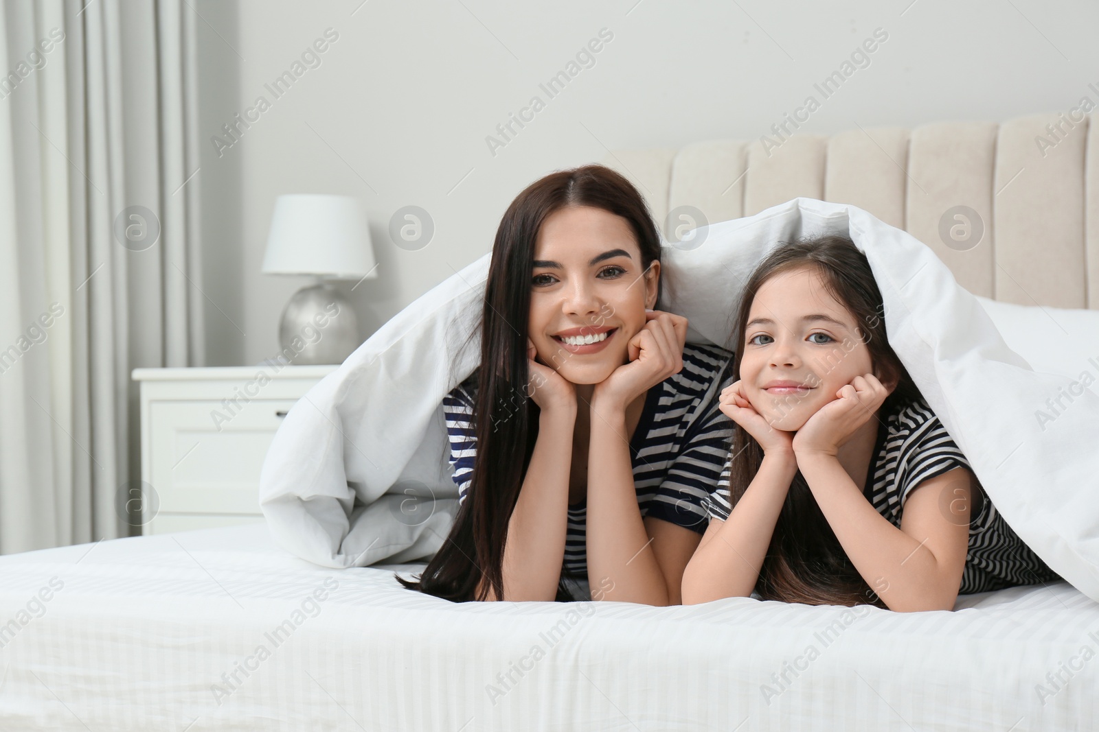 Photo of Young mother and her daughter under blanket in bed at home