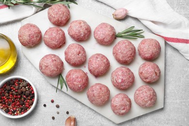 Many fresh raw meatballs and ingredients on light grey table, flat lay