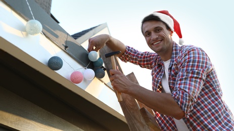 Man in Santa hat decorating house with Christmas lights outdoors