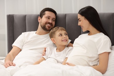 Happy pregnant woman with her son and husband in bed at home
