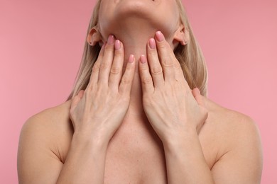 Woman touching her neck on pink background, closeup