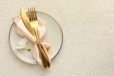 Stylish setting with cutlery, napkin, flower and plate on light textured table, top view. Space for text