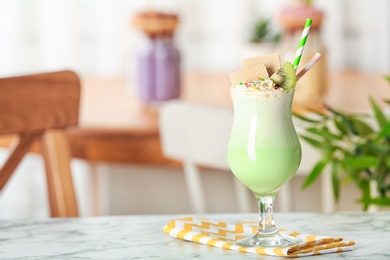 Glass with delicious milk shake on table against blurred background. Space for text