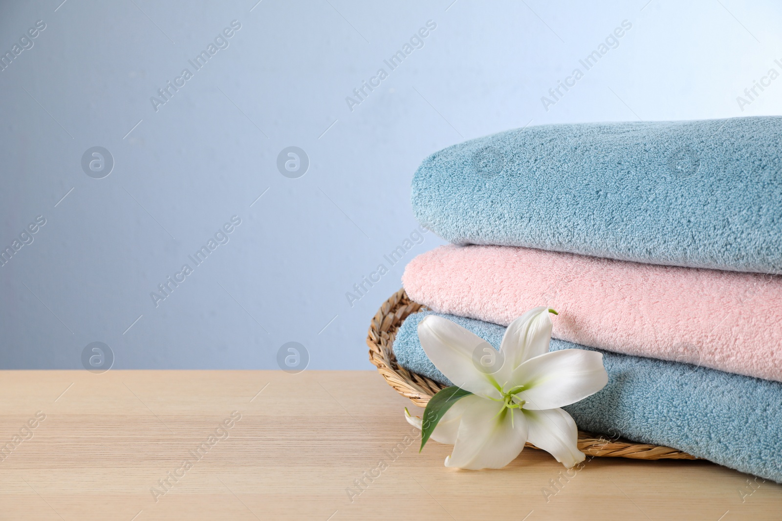 Photo of Stack of clean bath towels and beautiful flower on wooden table. Space for text
