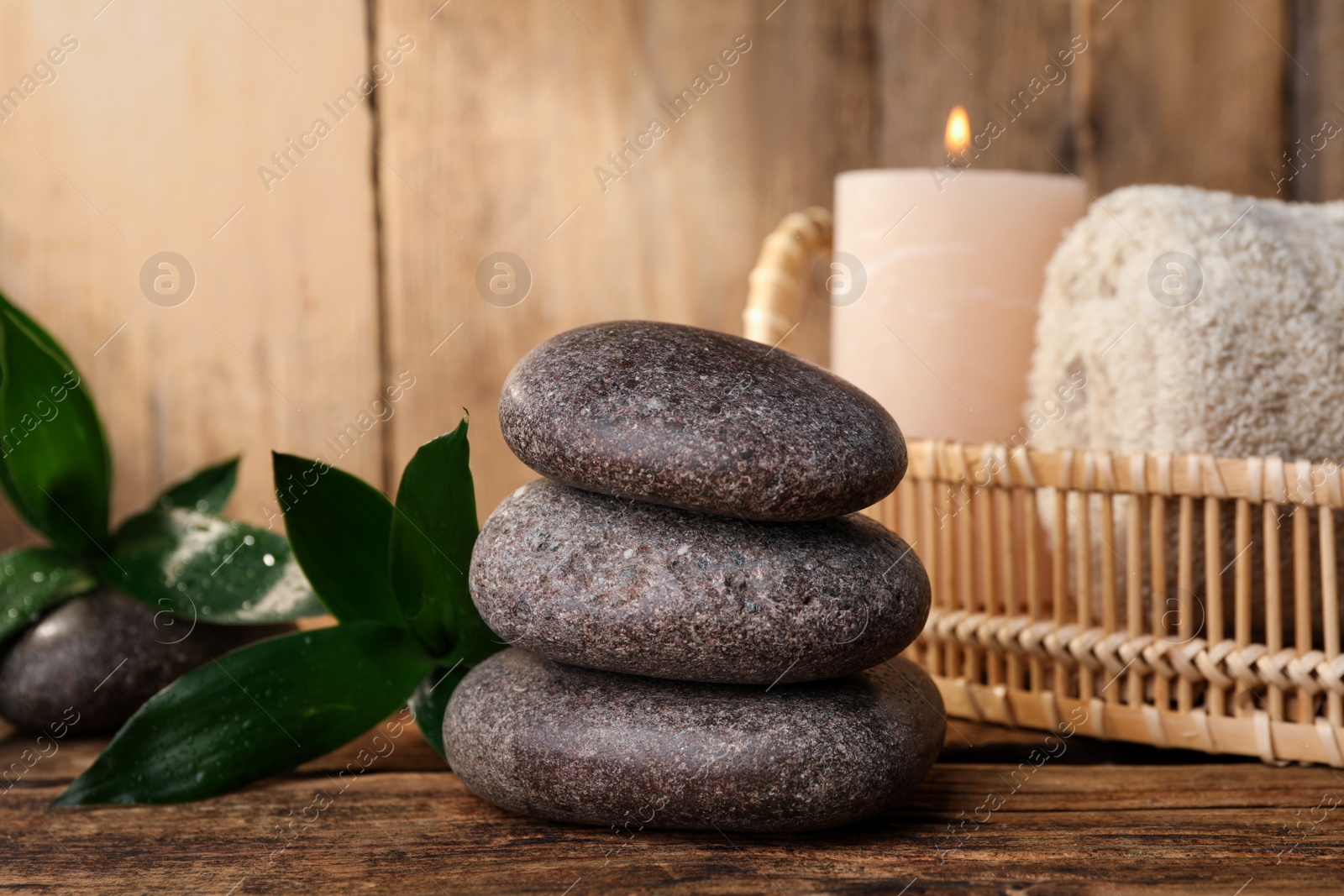 Photo of Stacked spa stones, bamboo leaves, candle and towel on wooden table. Space for text