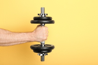 Photo of Male athlete holding metal dumbbell on color background. Space for text