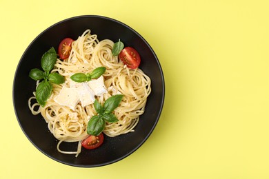 Bowl of delicious pasta with brie cheese, tomatoes and basil leaves on yellow background, top view. Space for text