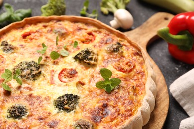 Delicious homemade vegetable quiche and oregano on black table, closeup