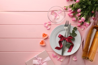 Place setting with heart shaped candles, bouquet of roses and gift for romantic dinner on pink wooden table, flat lay. Space for text