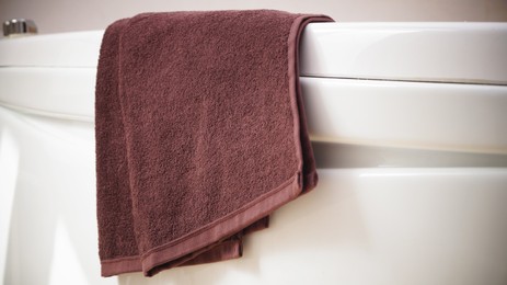 Photo of Brown soft towel on edge of bath indoors, closeup