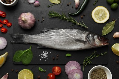 Photo of Sea bass fish and ingredients on black table, flat lay