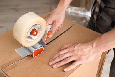 Photo of Young man packing moving box indoors, closeup