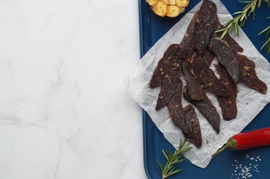 Photo of Pieces of delicious beef jerky and different spices on white marble table, top view. Space for text